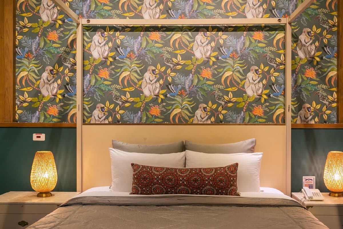 A hotel room with a canopy bed, patterned wallpaper, and two bedside lamps.