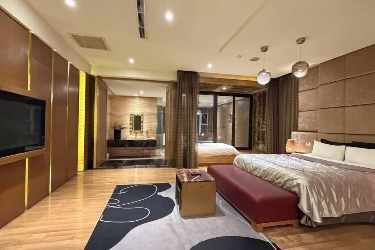 A modern hotel room with a large bed, a TV, a seating area, and a bathroom visible through an open door.