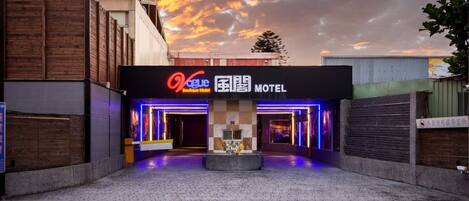 A motel with a neon sign, a checkered wall, and a paved entrance.