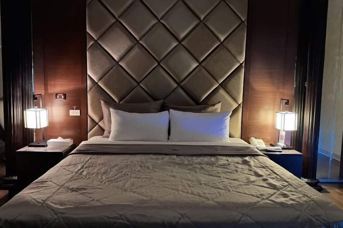 A hotel room with a large bed, a tufted headboard, two bedside tables with lamps, and a nightstand.