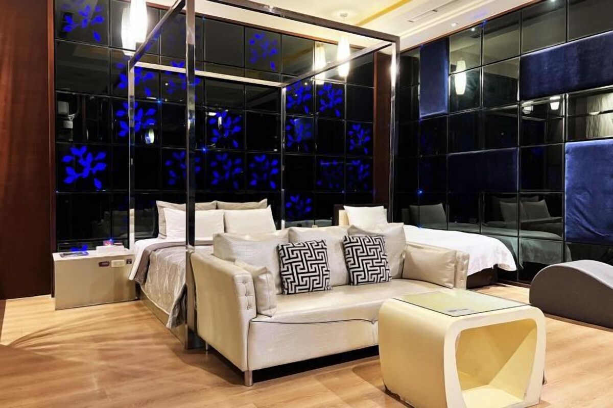 A modern hotel room with a sofa bed, a small table, and a glass partition with blue floral patterns.