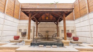 Um pátio externo com pérgola de madeira, duas cadeiras e dois grandes vasos vermelhos sobre pedestais.