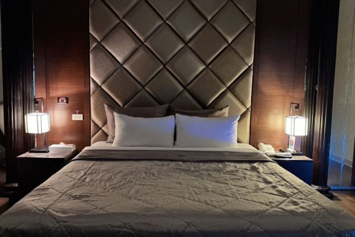 A hotel room with a large bed, a tufted headboard, two bedside tables with lamps, and a nightstand.