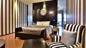 Quarto de hotel moderno com uma cama grande, um sofá de couro preto, uma poltrona listrada e um espelho de parede exclusivo.