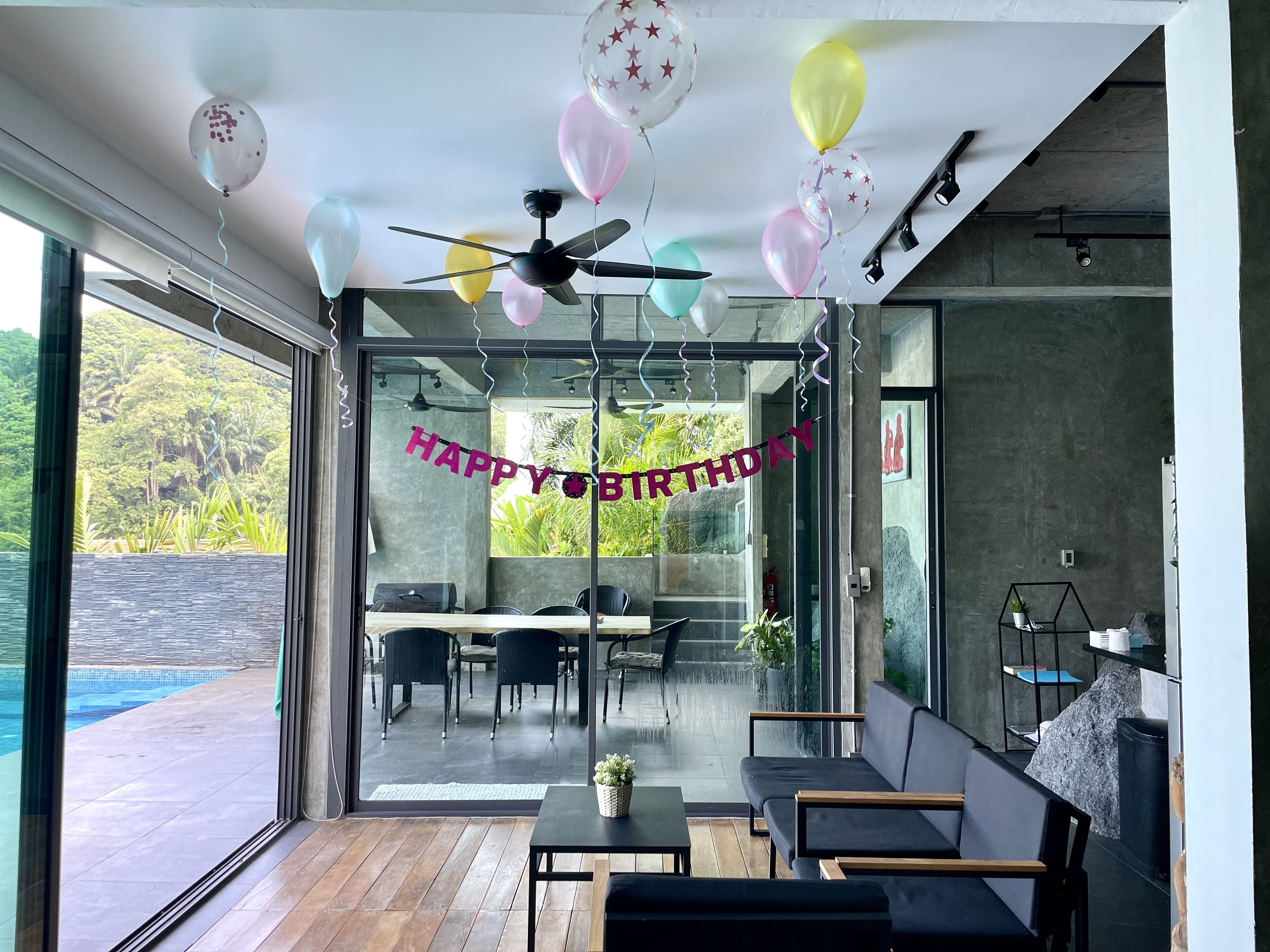 Decoração moderna com parede de vidro, ventilador de teto e um letreiro de 'FELIZ ANIVERSÁRIO'.