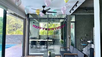 Decoração moderna com parede de vidro, ventilador de teto e um letreiro de 'FELIZ ANIVERSÁRIO'.