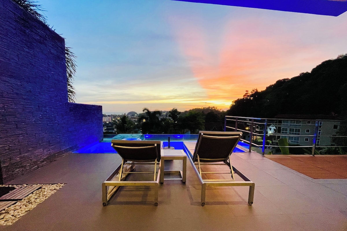 Una terraza en la azotea con dos sillones de descanso, una piscina y vistas a la ciudad al atardecer.