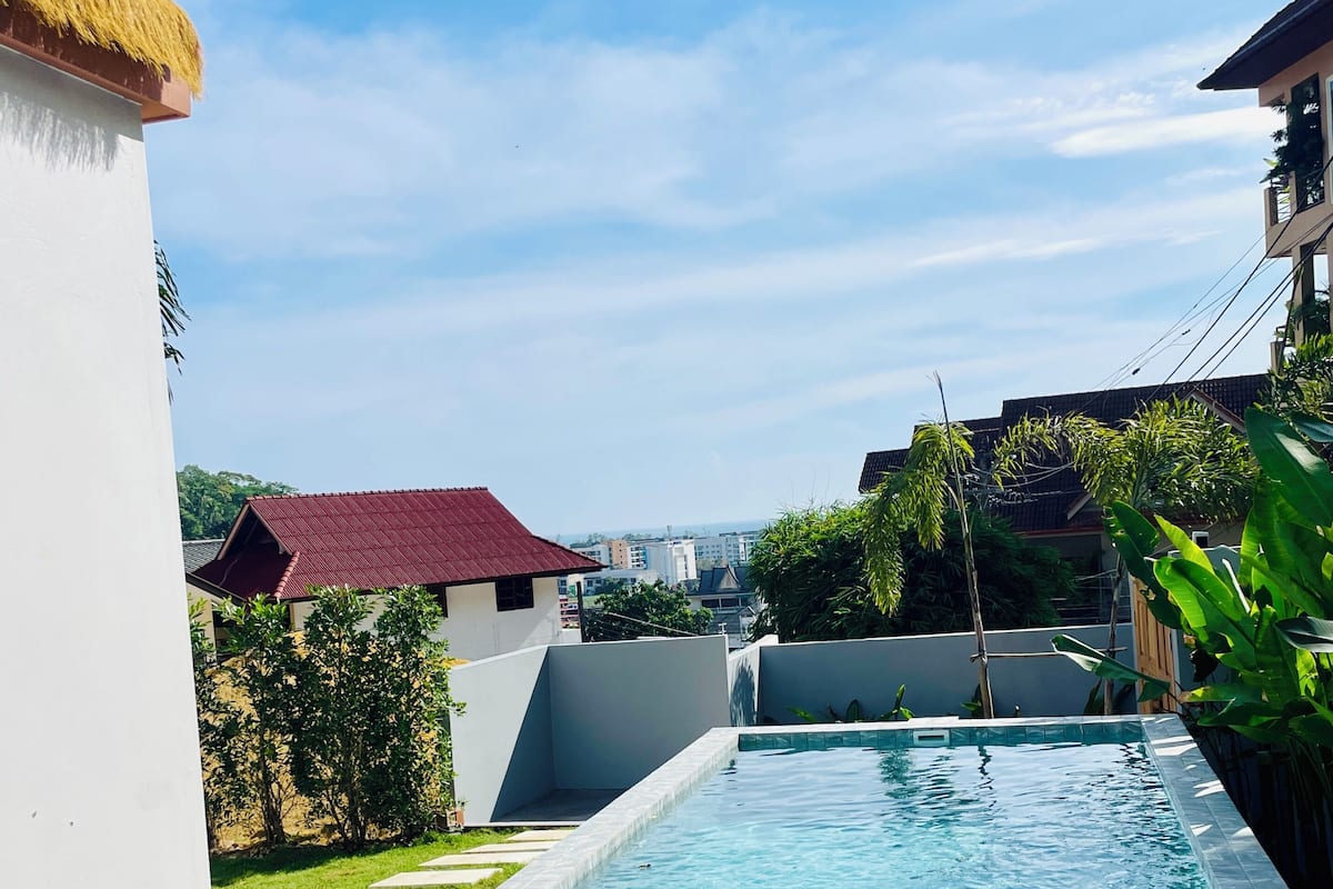 Una piscina con superficie de agua azul cristalina, rodeada por un muro blanco y un edificio de techo rojo al fondo.