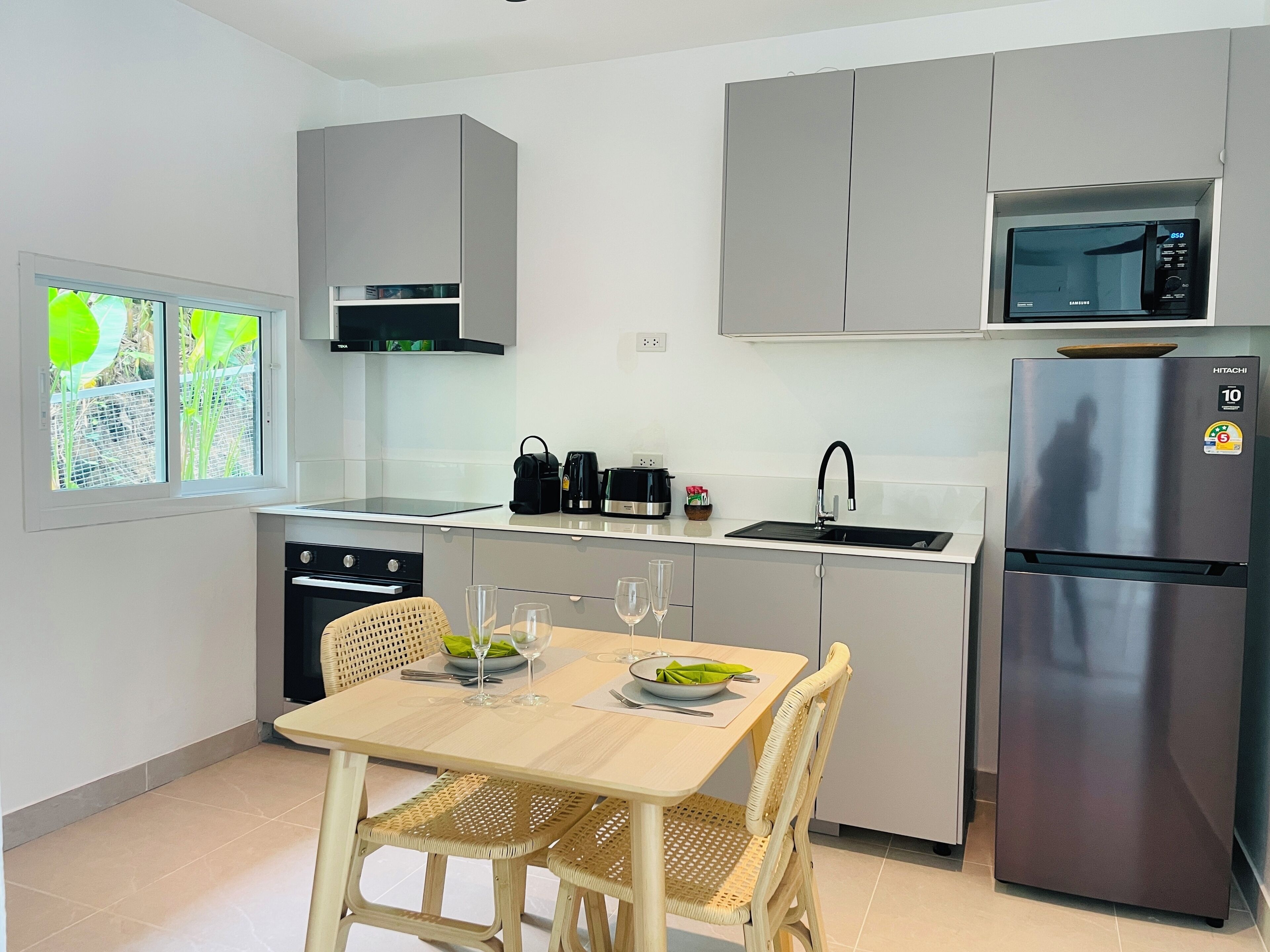 A modern kitchen with grey cabinets, a stainless steel refrigerator, a microwave, and a dining area with a table and chairs.