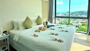 Ein Hotelzimmer mit einem großen Bett, Blick auf eine Stadtansicht und einem mit Vorhängen versehenen Fenster.