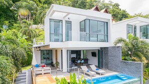 Ein modernes, zweistöckiges Haus mit Swimmingpool, Sitzgelegenheiten im Freien und üppiger Bepflanzung.
