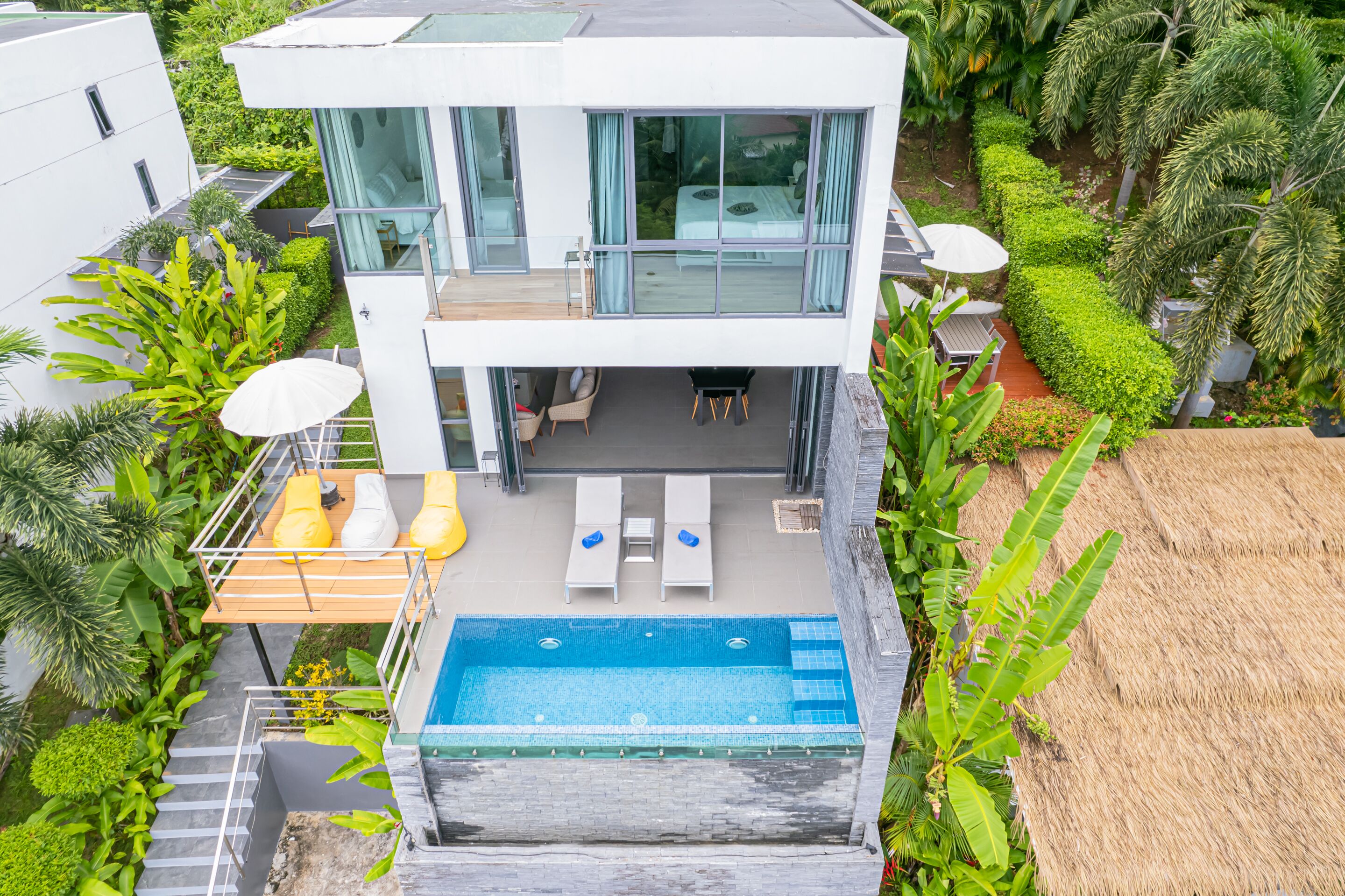 Ein modernes, zweistöckiges Haus mit Swimmingpool, Sitzgelegenheiten im Freien und üppiger Bepflanzung.