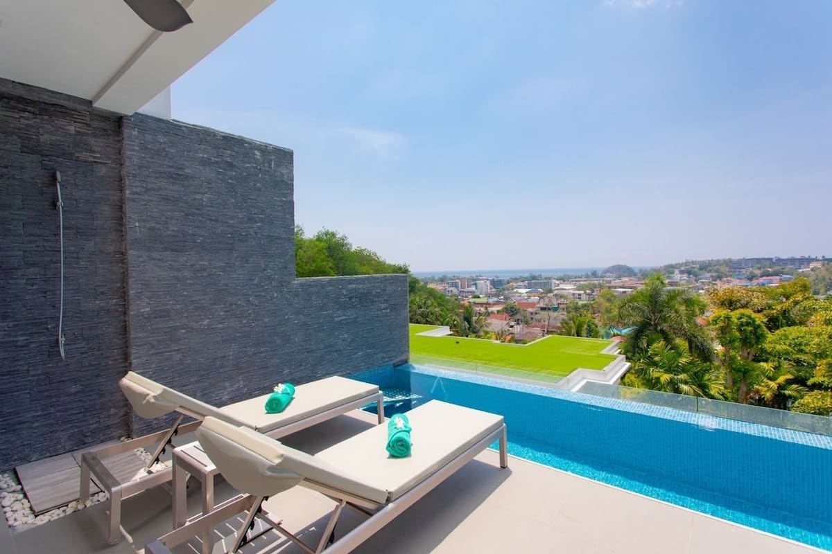 Un área de piscina exterior moderna con sillones de descanso y vistas a un paisaje urbano.