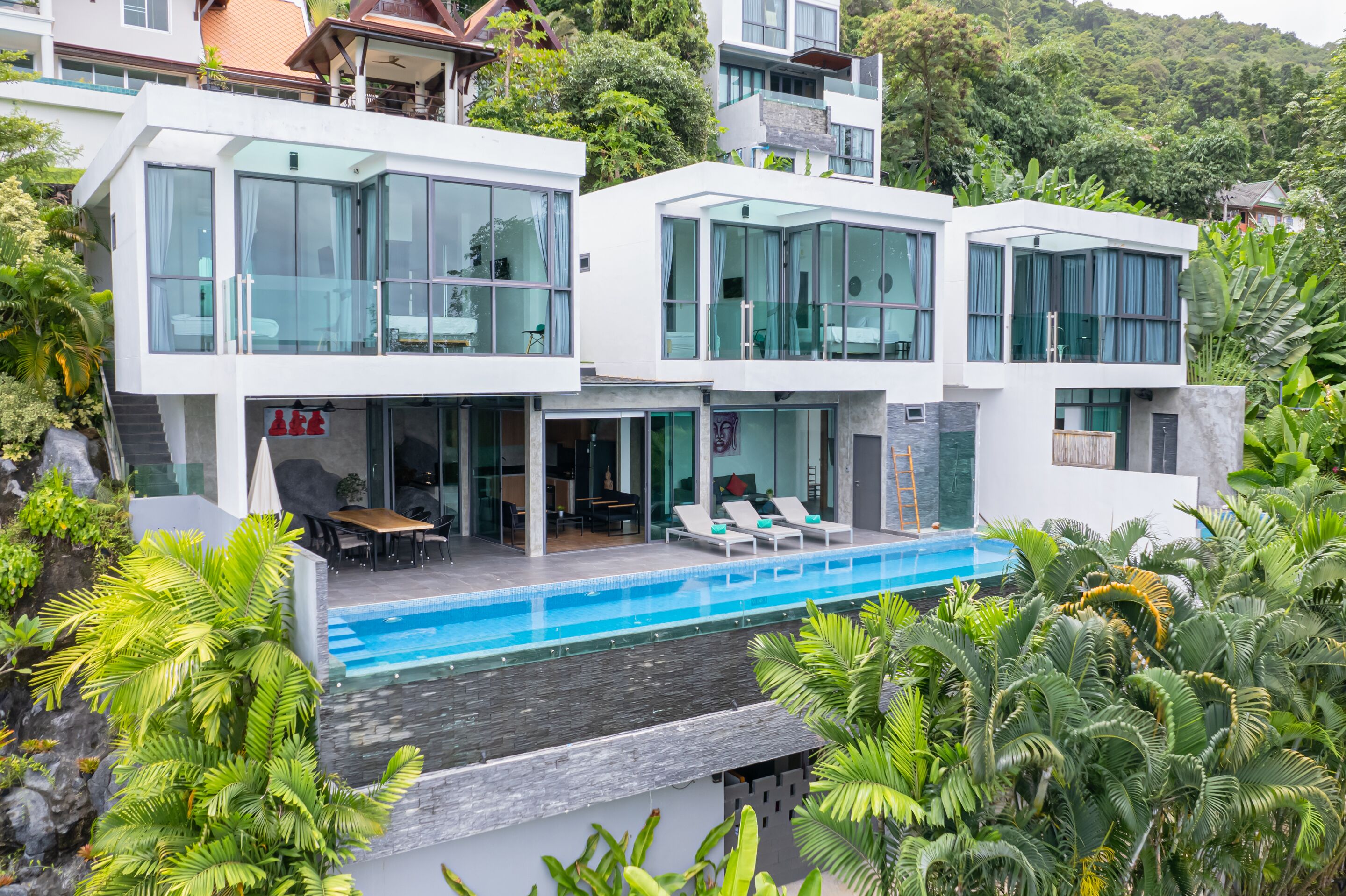 A modern two-story house with a swimming pool, surrounded by lush greenery.