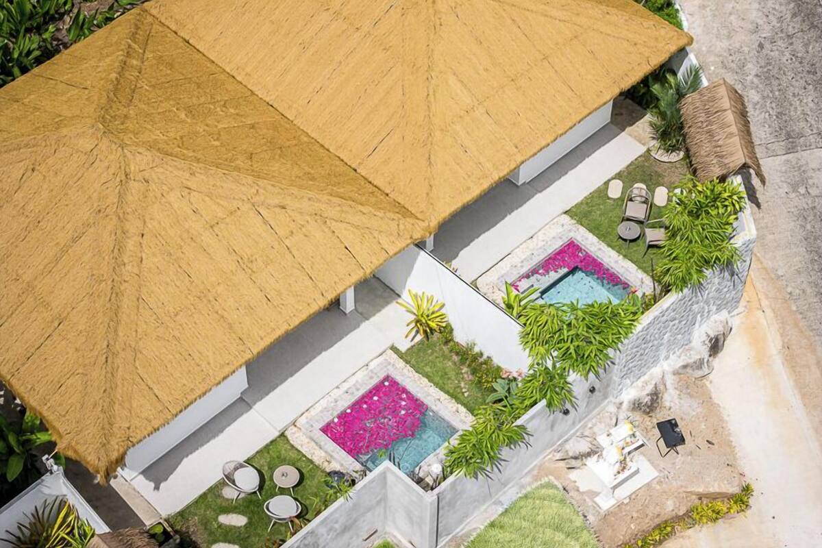 Una casa moderna con un amplio techo de paja, piscina y jardín con mobiliario exterior.