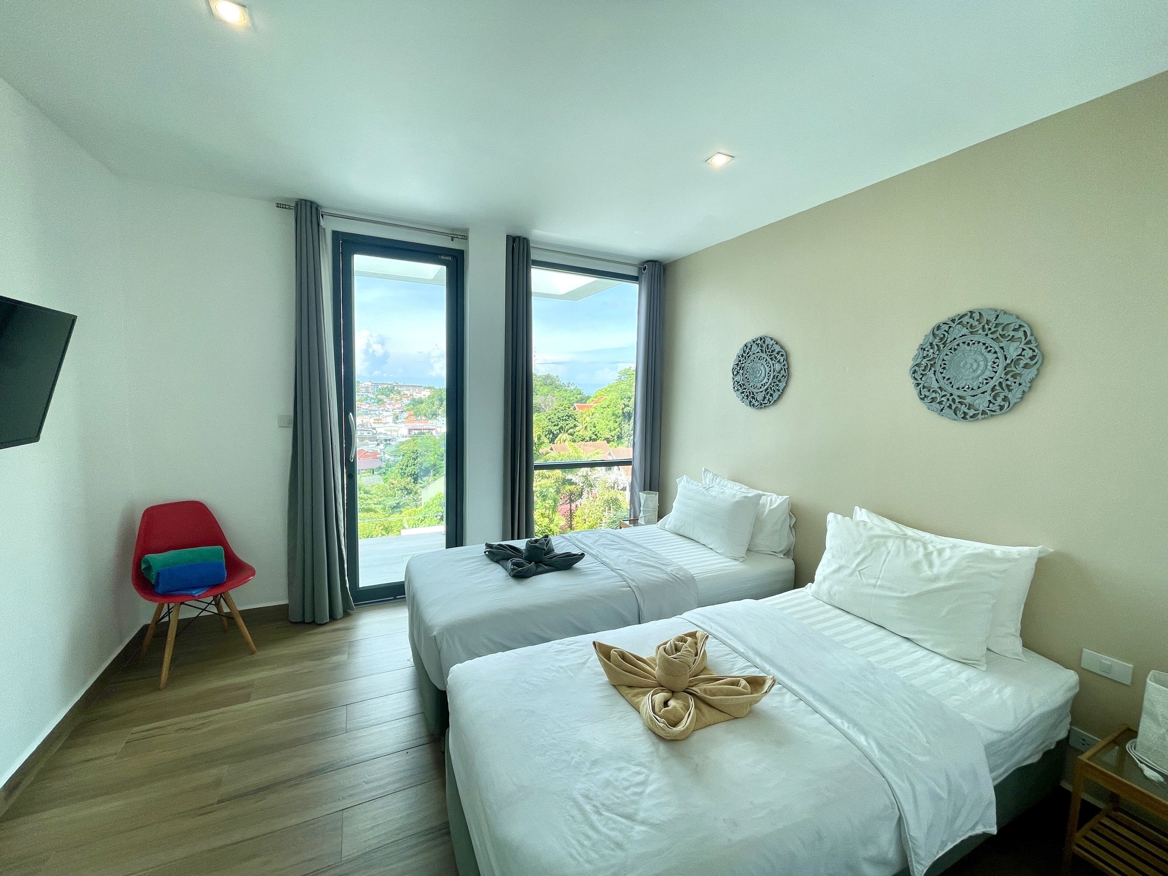 Une chambre d’hôtel avec deux lits, une télévision, un fauteuil rouge et un balcon donnant sur la ville.