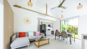 Ein modernes Wohnzimmer mit einer Couch, einem Couchtisch, einem Esstisch und Stühlen. Im Hintergrund ist eine Küche mit Kühlschrank und Mikrowelle zu sehen.