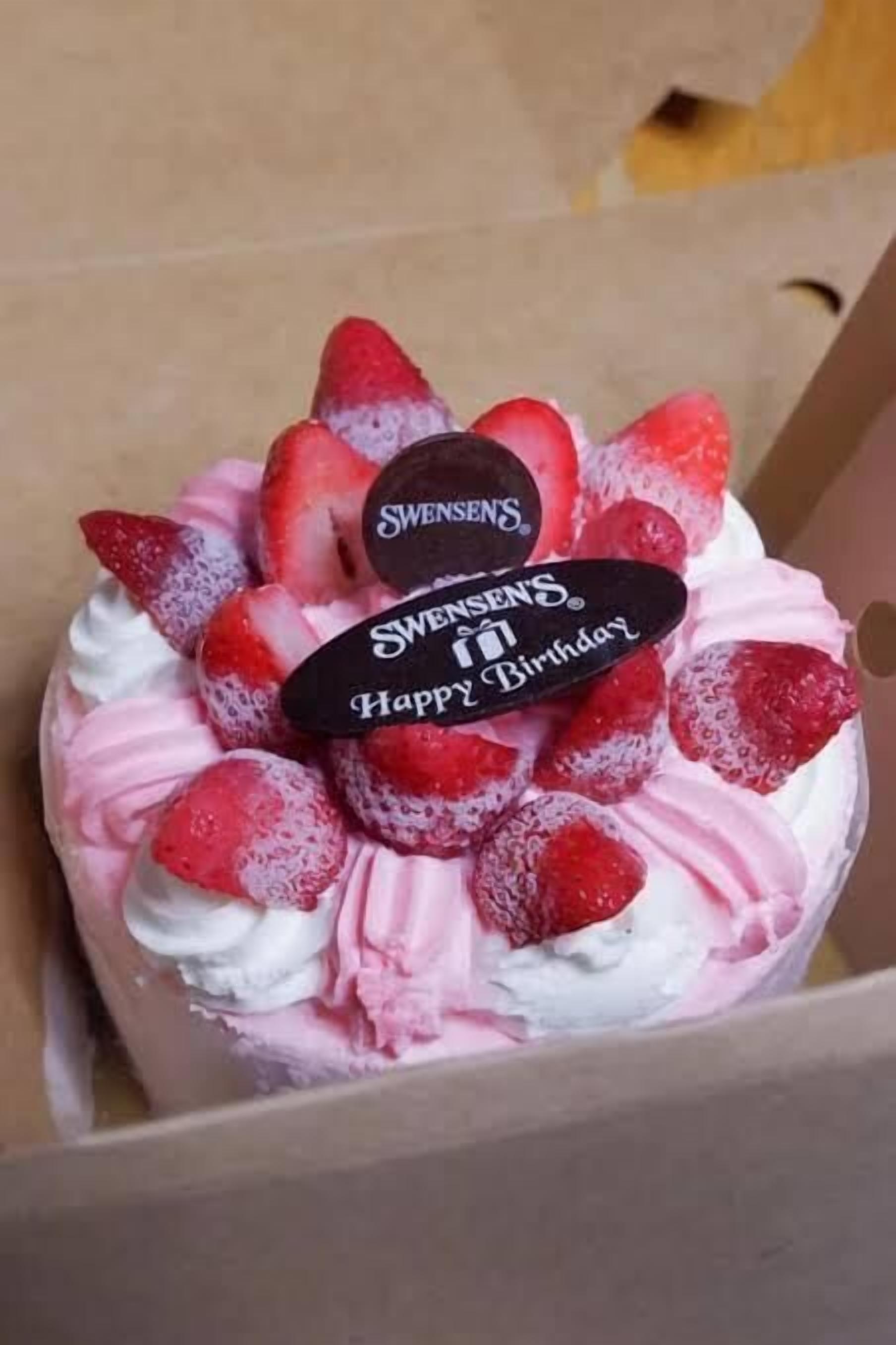 Un gâteau d’anniversaire aux fraises, surmonté d’une décoration « Joyeux anniversaire de Swensen’s », le tout présenté dans une boîte en carton.