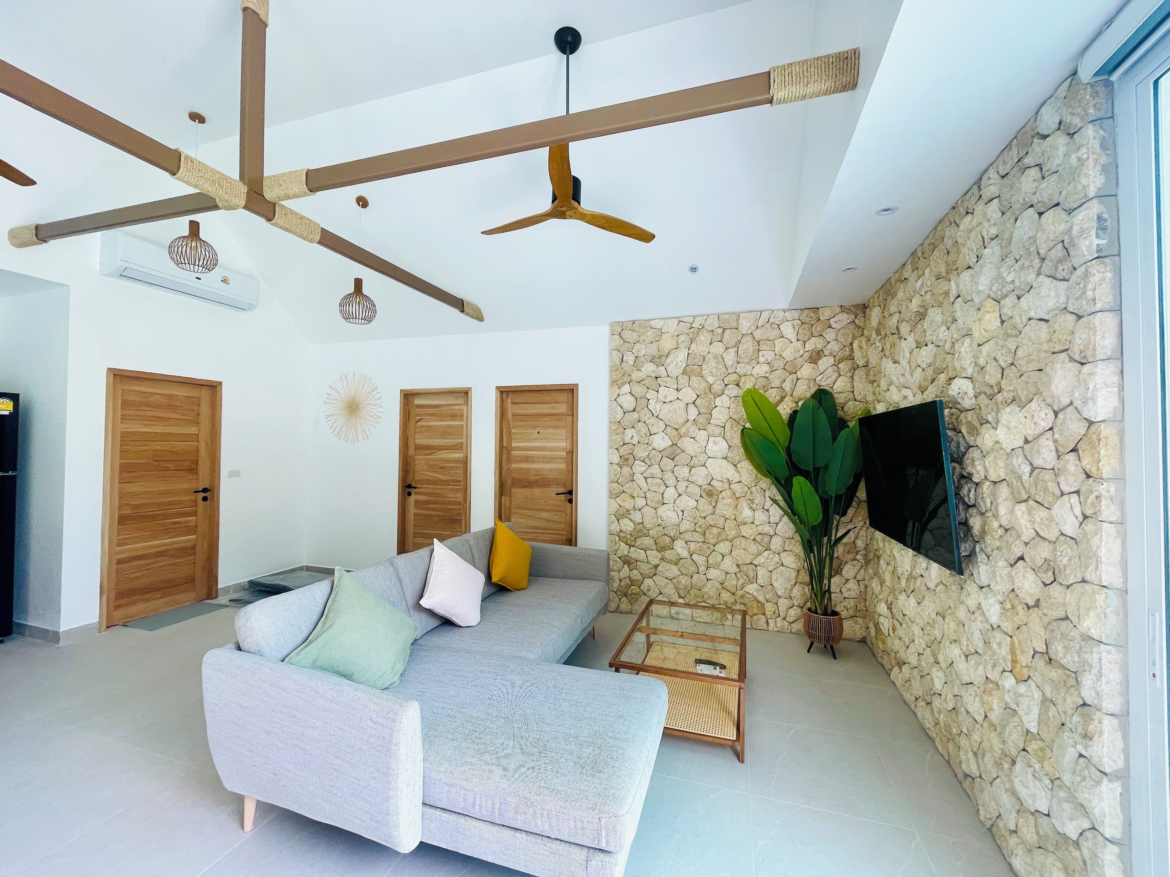 A modern living room with a grey sofa, wooden doors, a stone wall, and a ceiling fan.