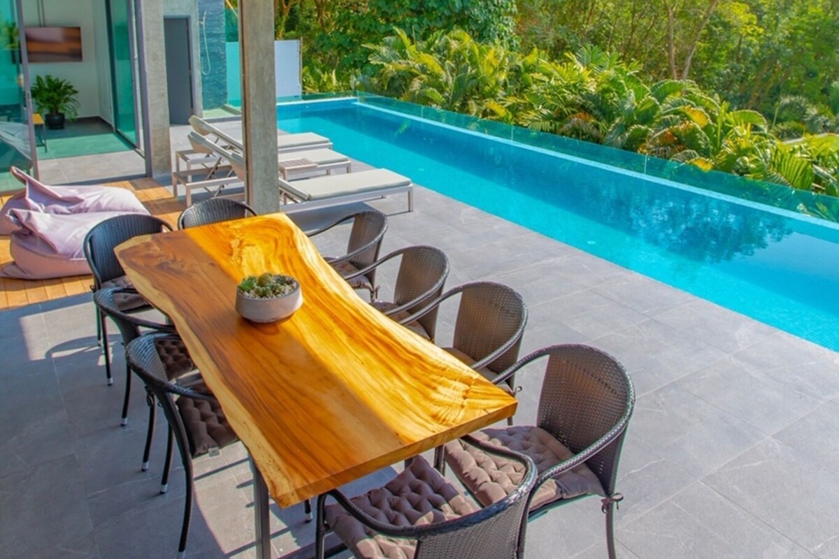 A covered outdoor area with a pool, lounge chairs, and a wooden table.