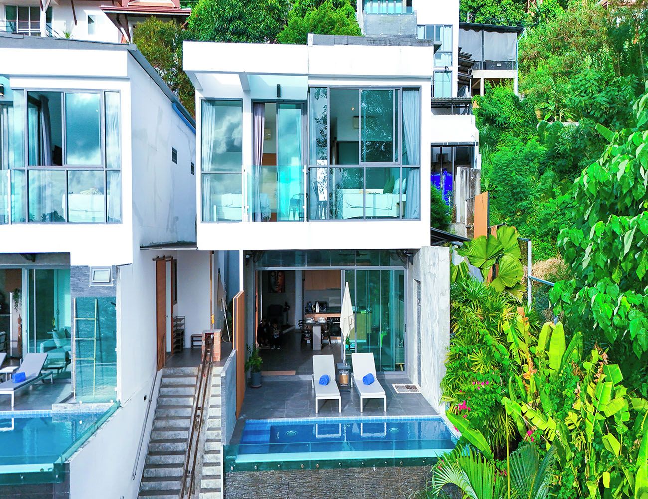 Una casa moderna de varios pisos con fachada de vidrio, piscina y un jardín exuberante.