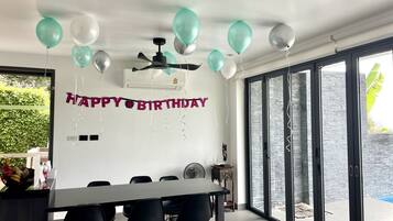 Een moderne eethoek met een zwarte tafel en stoelen, een plafondventilator en een 'Happy Birthday' spandoek.
