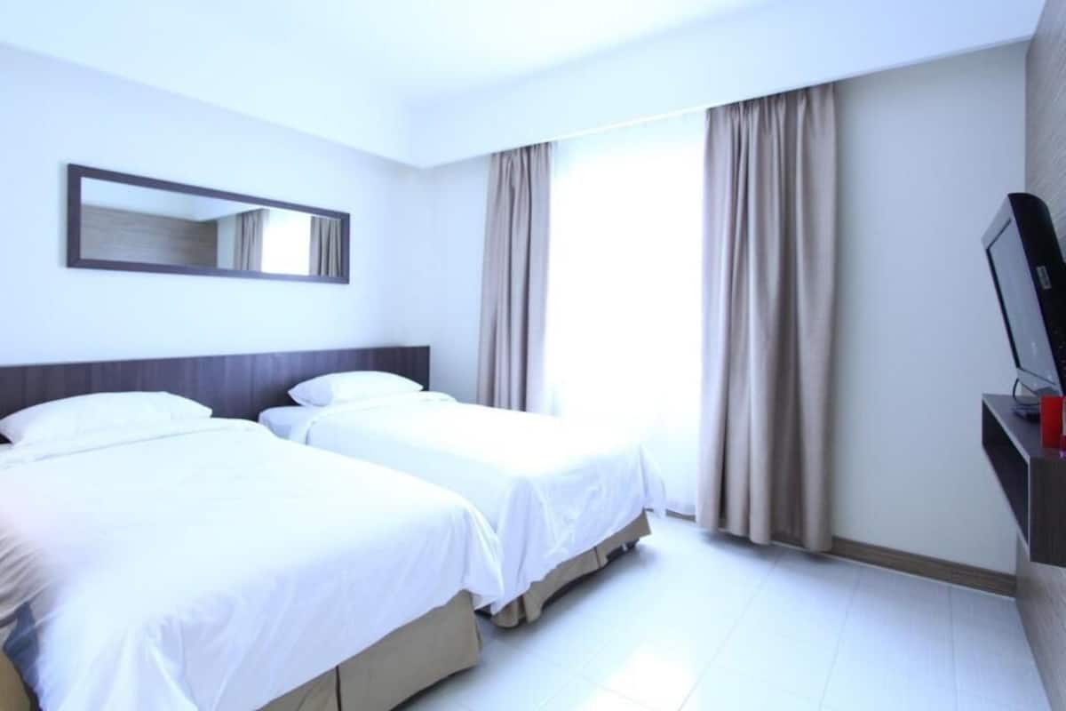 A hotel room with two beds, a TV, a mirror, and a window with curtains.