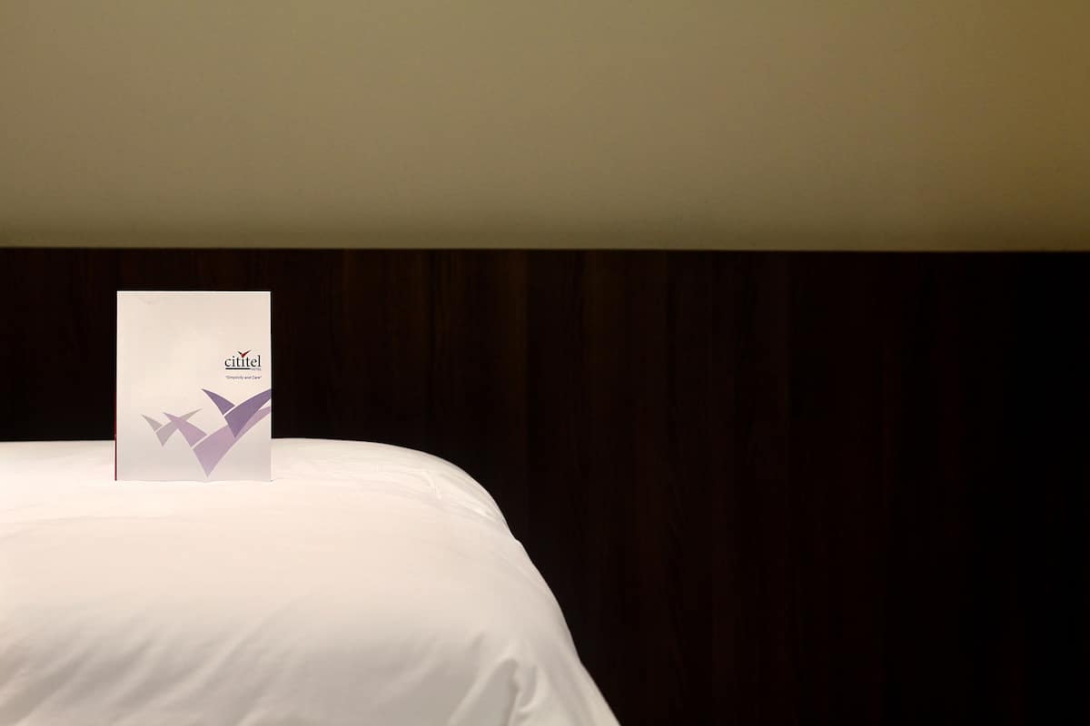 A neatly made bed with a white bedspread and a sign on it that reads "cittel".