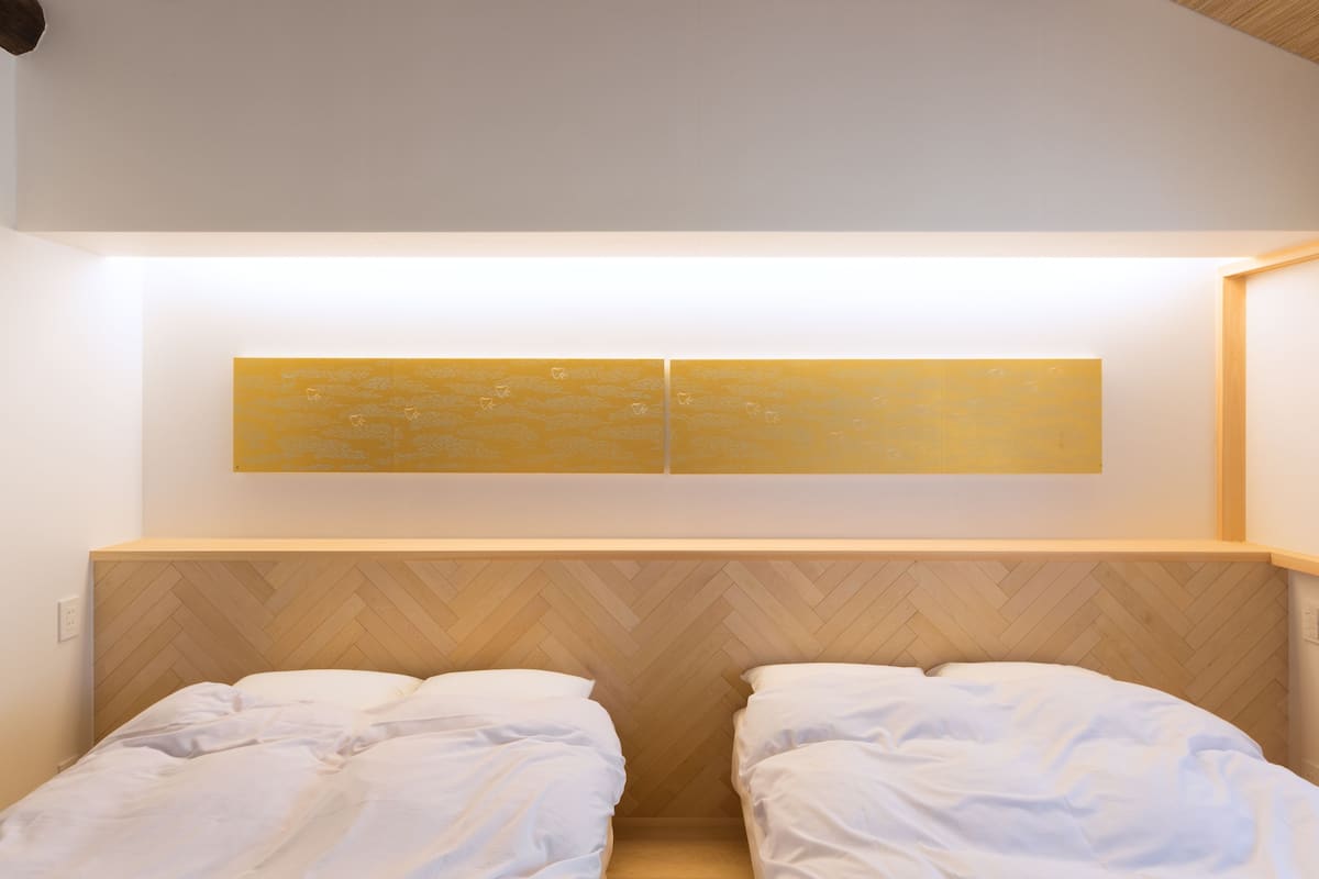 A bedroom with two beds, a wooden herringbone headboard, and a wall-mounted light fixture.