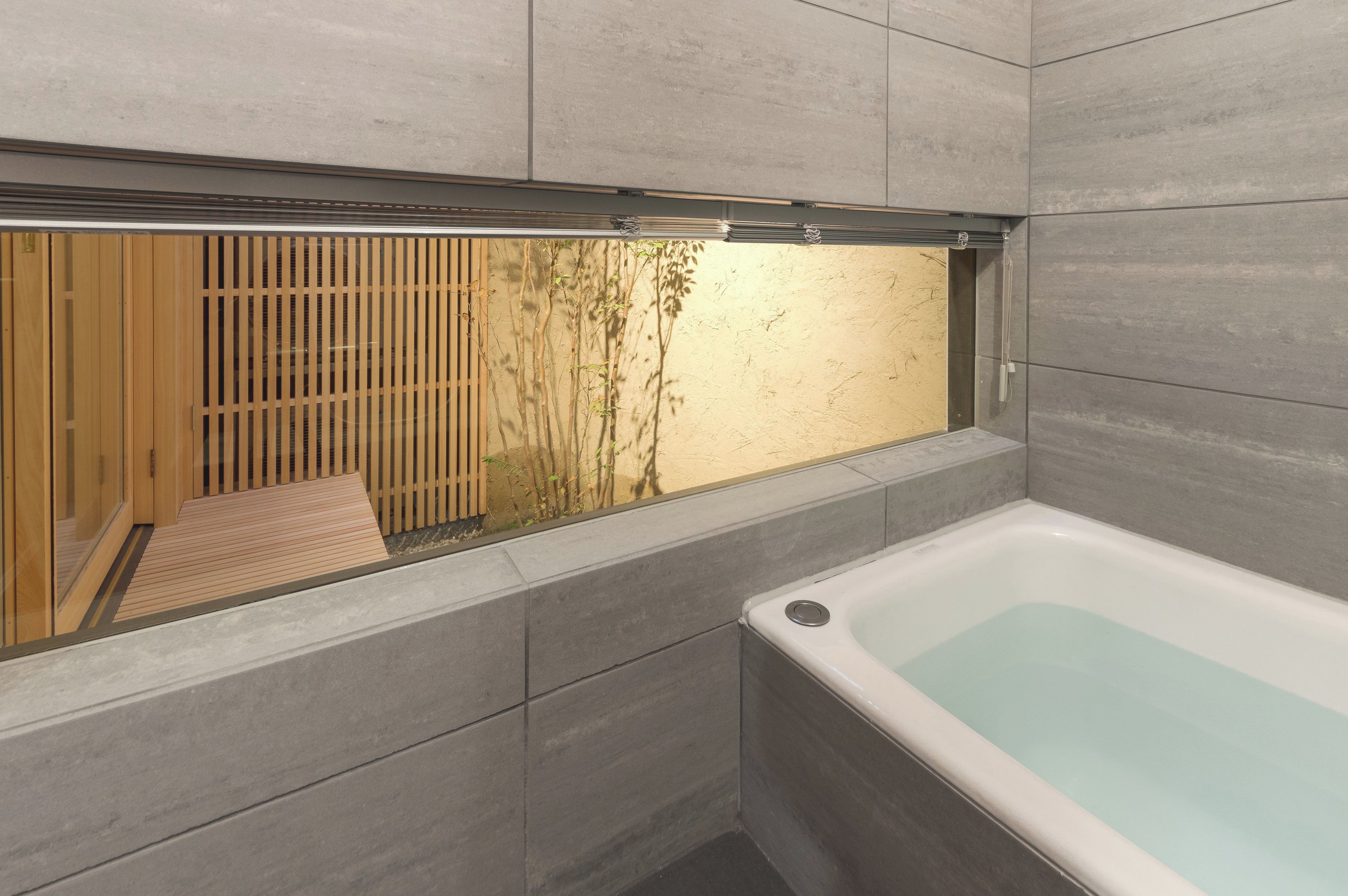 A modern bathroom with a bathtub, a wooden sliding door, and a view of a garden.