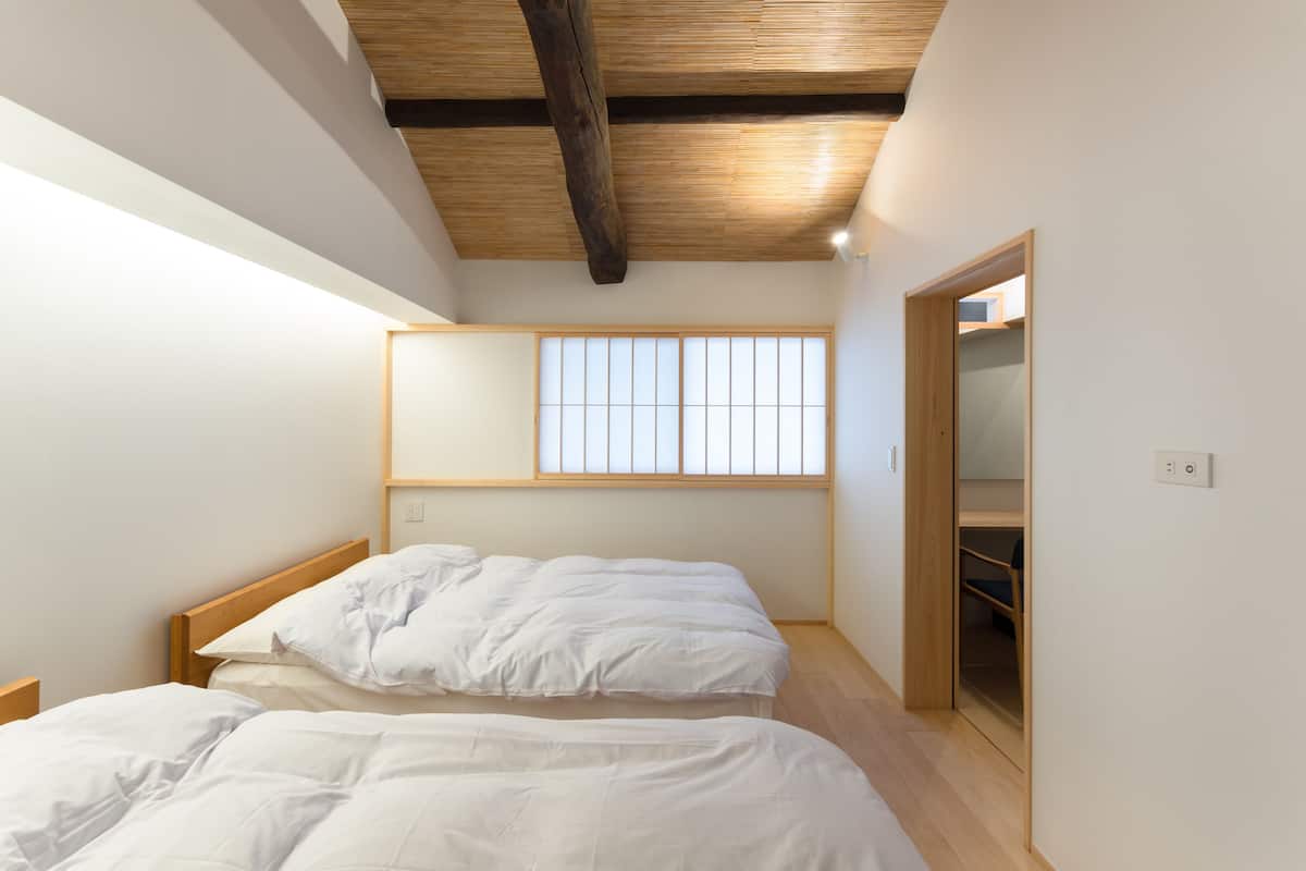 A bedroom with two beds, a wooden ceiling, a window with a grid pattern, and a built-in wardrobe.
