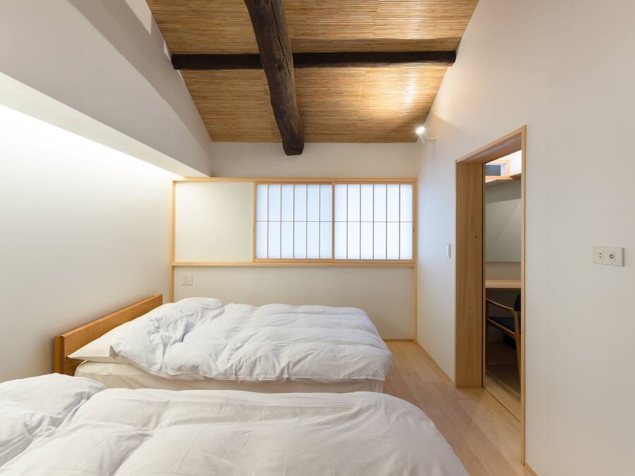 A bedroom with two beds, a wooden ceiling, a window with a grid pattern, and a built-in wardrobe.