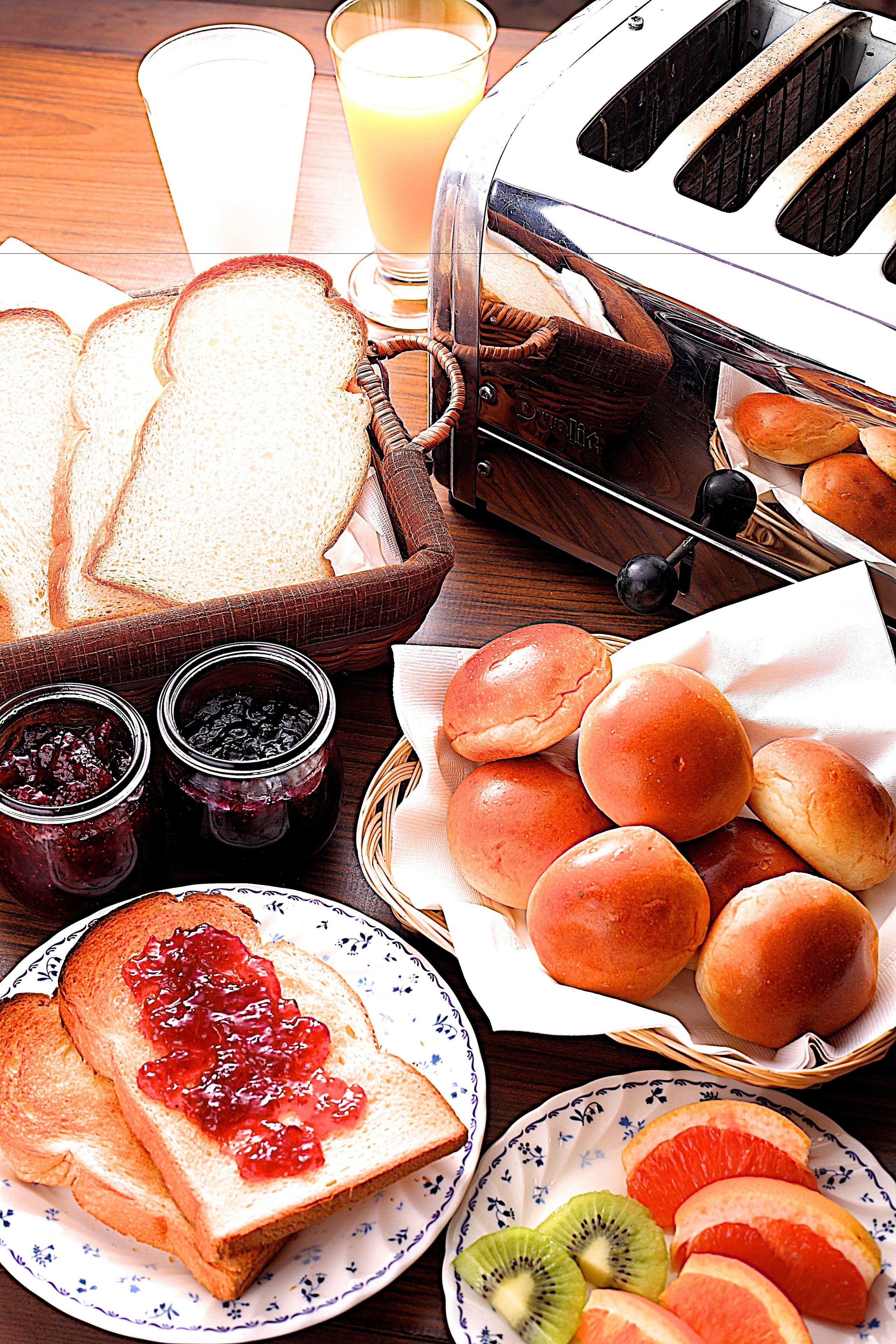 A breakfast setting with bread, toast, jam, rolls, and fruit on a wooden table.