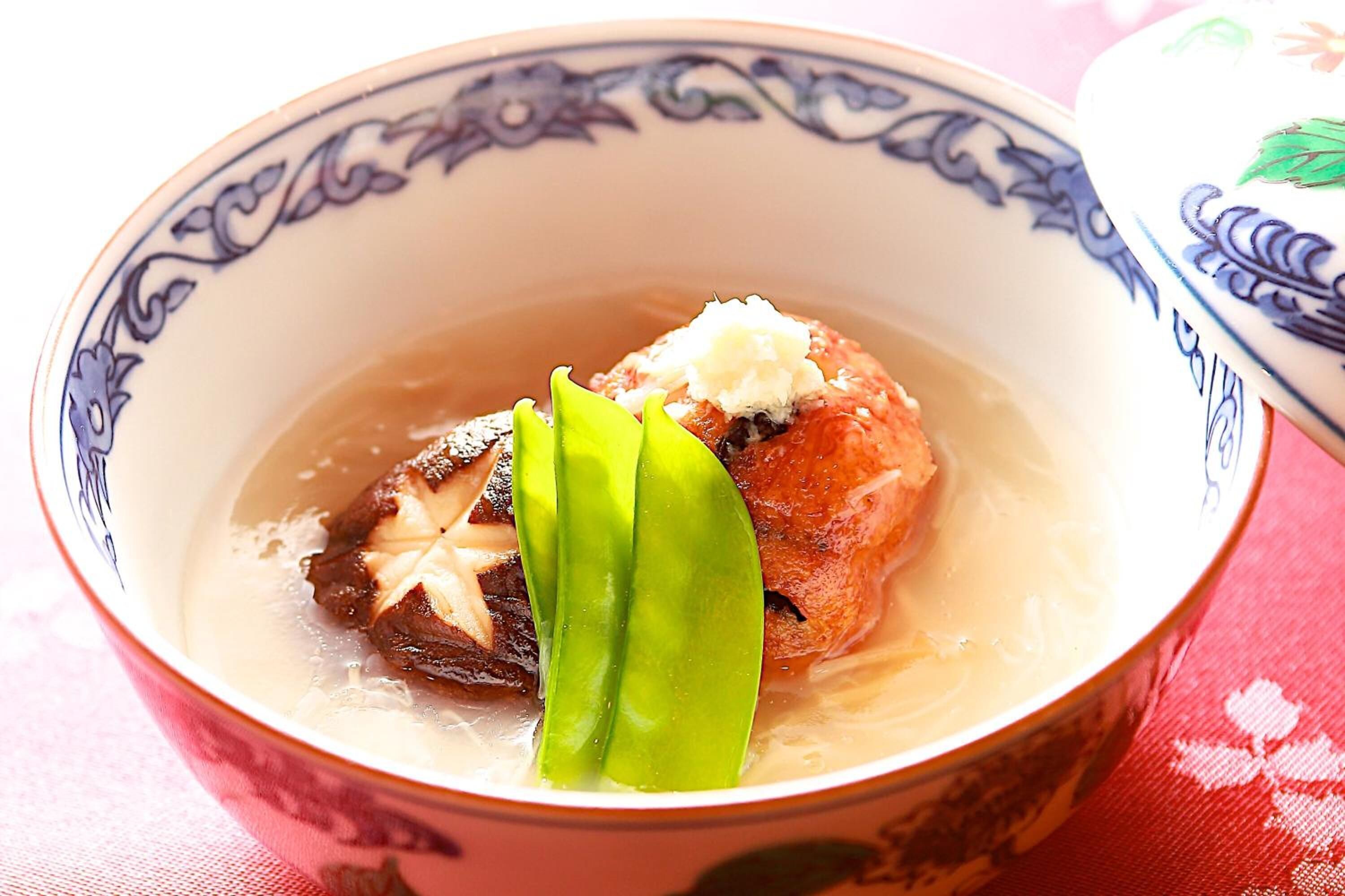 A bowl with a decorative pattern, containing a piece of food and green leaves.
