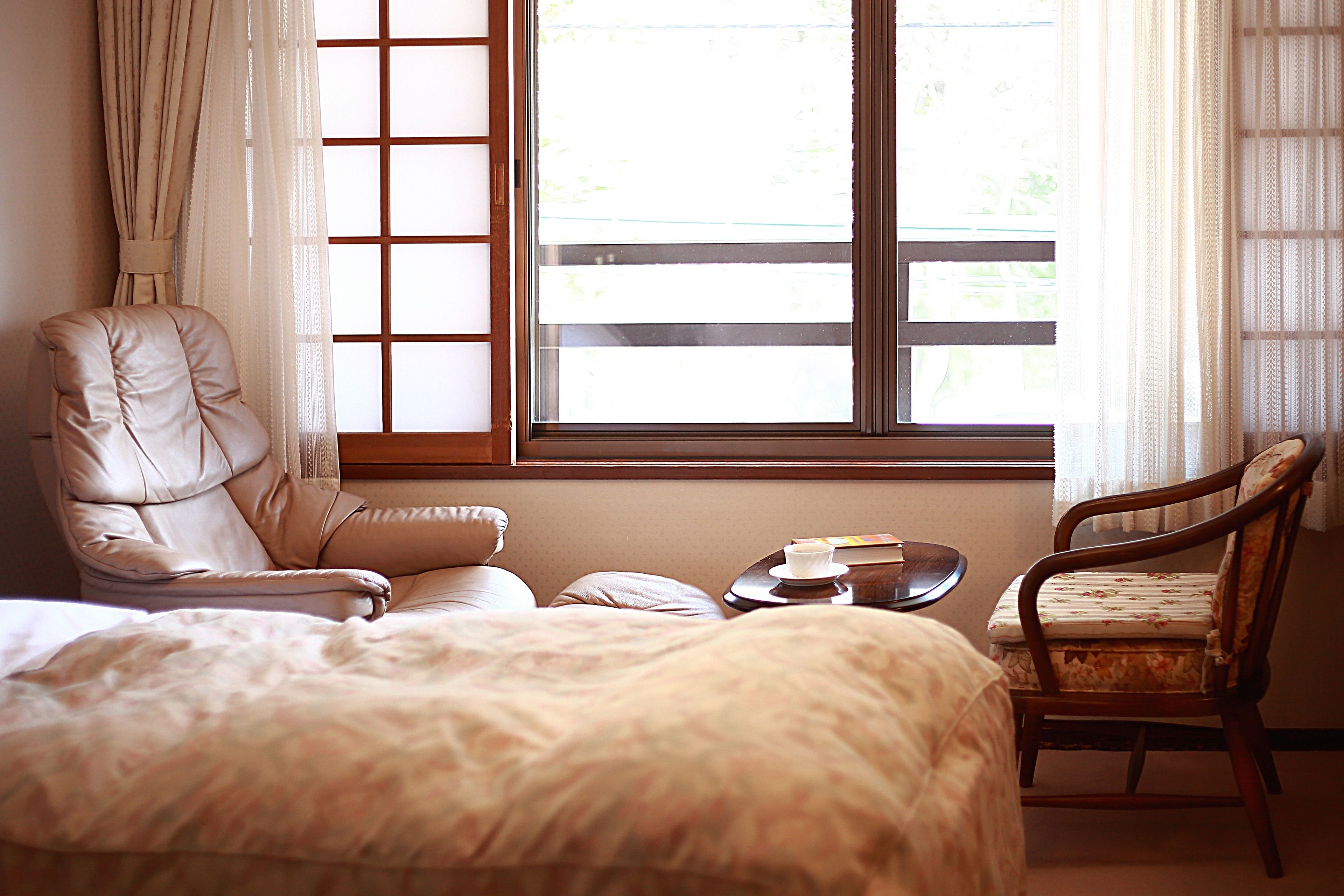 A bedroom with a large bed, a leather armchair, a wooden chair, and a small table with a book and a cup.