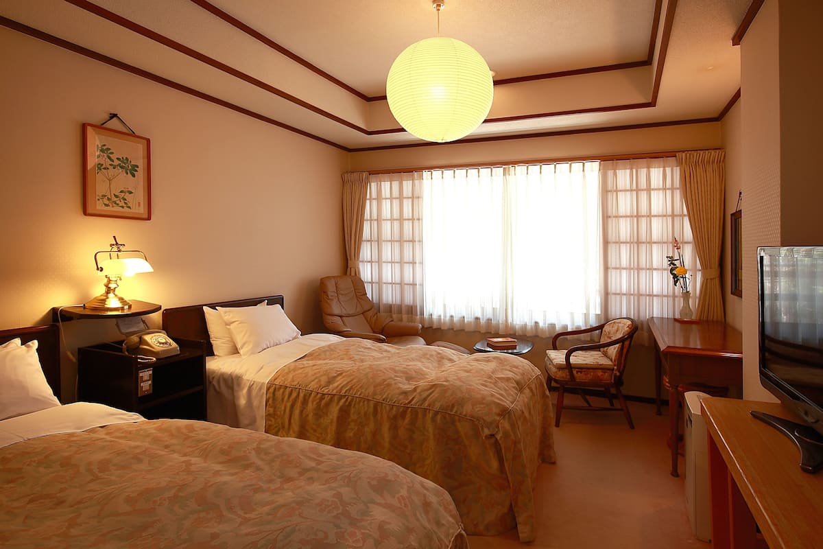 Une chambre d’hôtel avec deux lits, un bureau avec une télévision, une chaise et une lampe.
