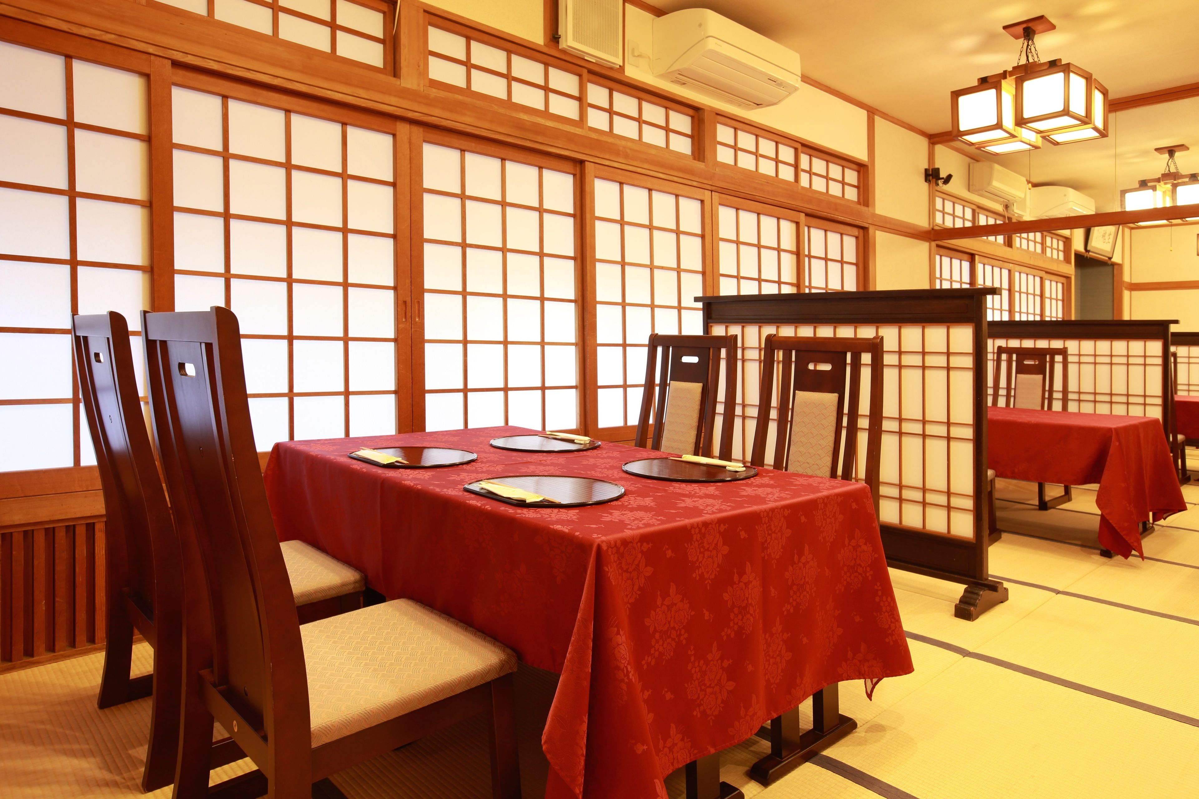 A traditional Japanese room with tatami mat flooring, wooden sliding doors, and a table set with a red tablecloth.