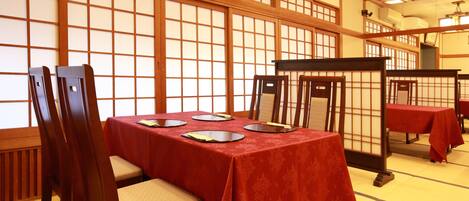A traditional Japanese room with tatami mat flooring, wooden sliding doors, and a table set with a red tablecloth.