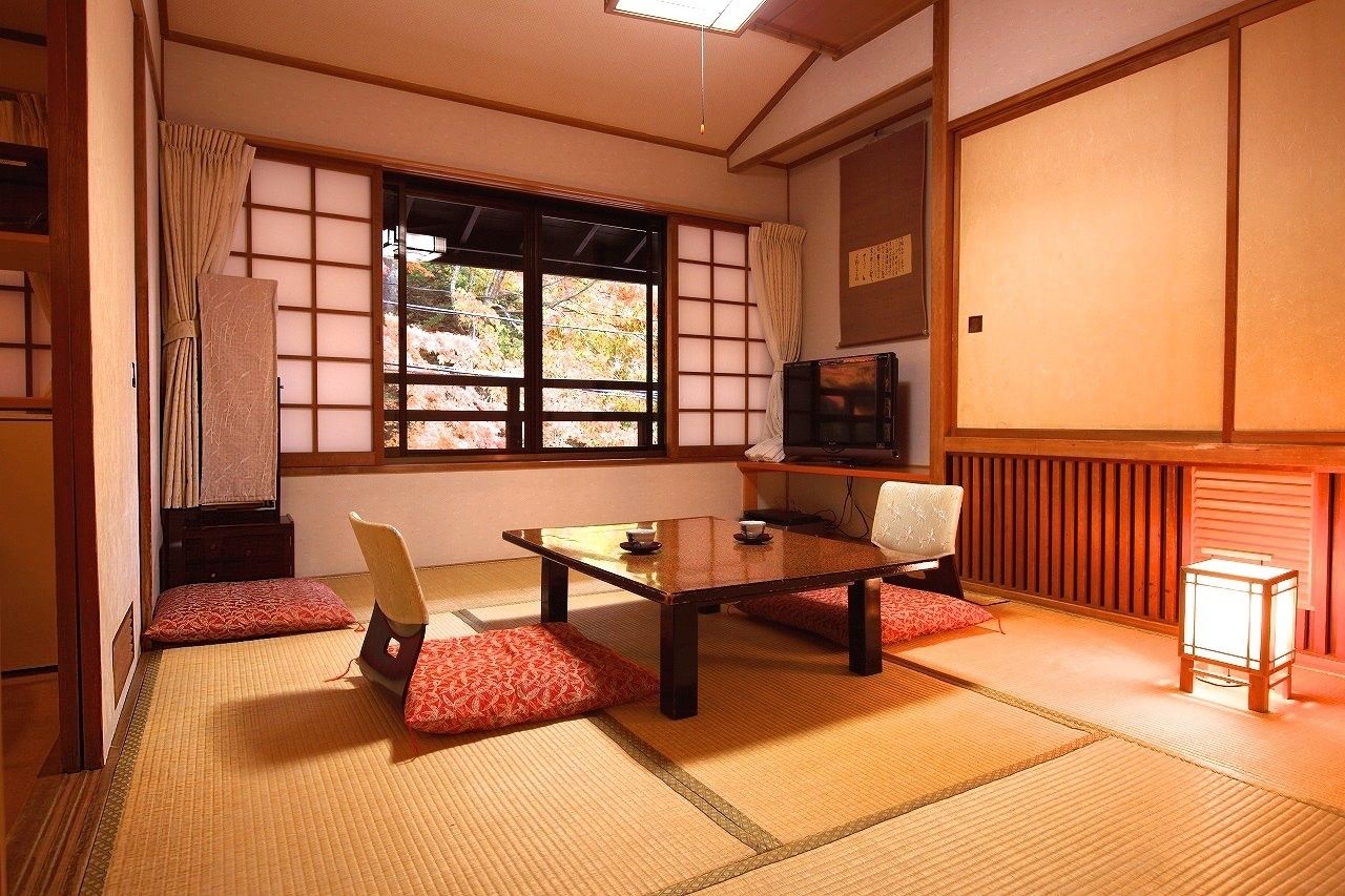 A traditional Japanese room with tatami flooring, a low table, two chairs, a television, and a sliding door.