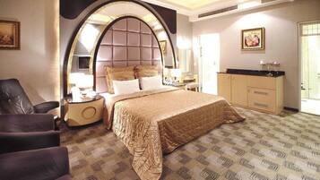 A hotel room with a large bed, a vanity with a mirror, a chair, and a desk.