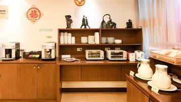 A hotel kitchen with wooden cabinets, a coffee station, a buffet area with plates and bowls, and a decorative wall hanging.