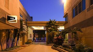 A hotel entrance with a sign indicating room number 102, a covered walkway, and decorative plants.