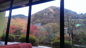 A view through large windows of a room with a view of a hillside covered in autumn foliage. - Matsuriya Yuzaemon (Fukushima)