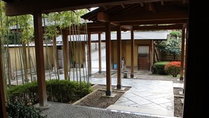 A covered outdoor area with a tiled floor, bamboo plants, and a small garden with a red bush. - Matsuriya Yuzaemon (Fukushima)