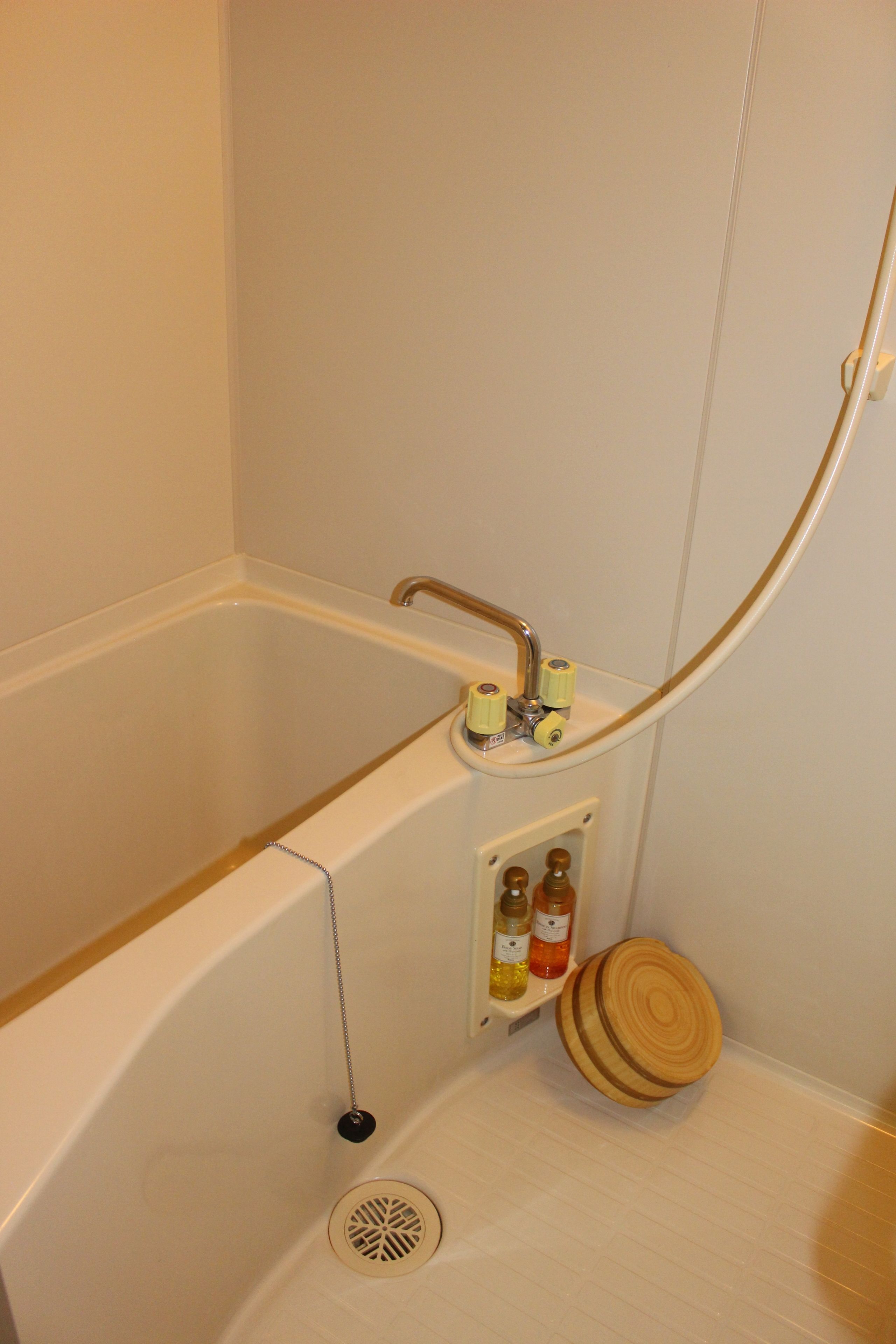 Une salle de bain avec une baignoire, une pomme de douche et une étagère remplie de bouteilles.