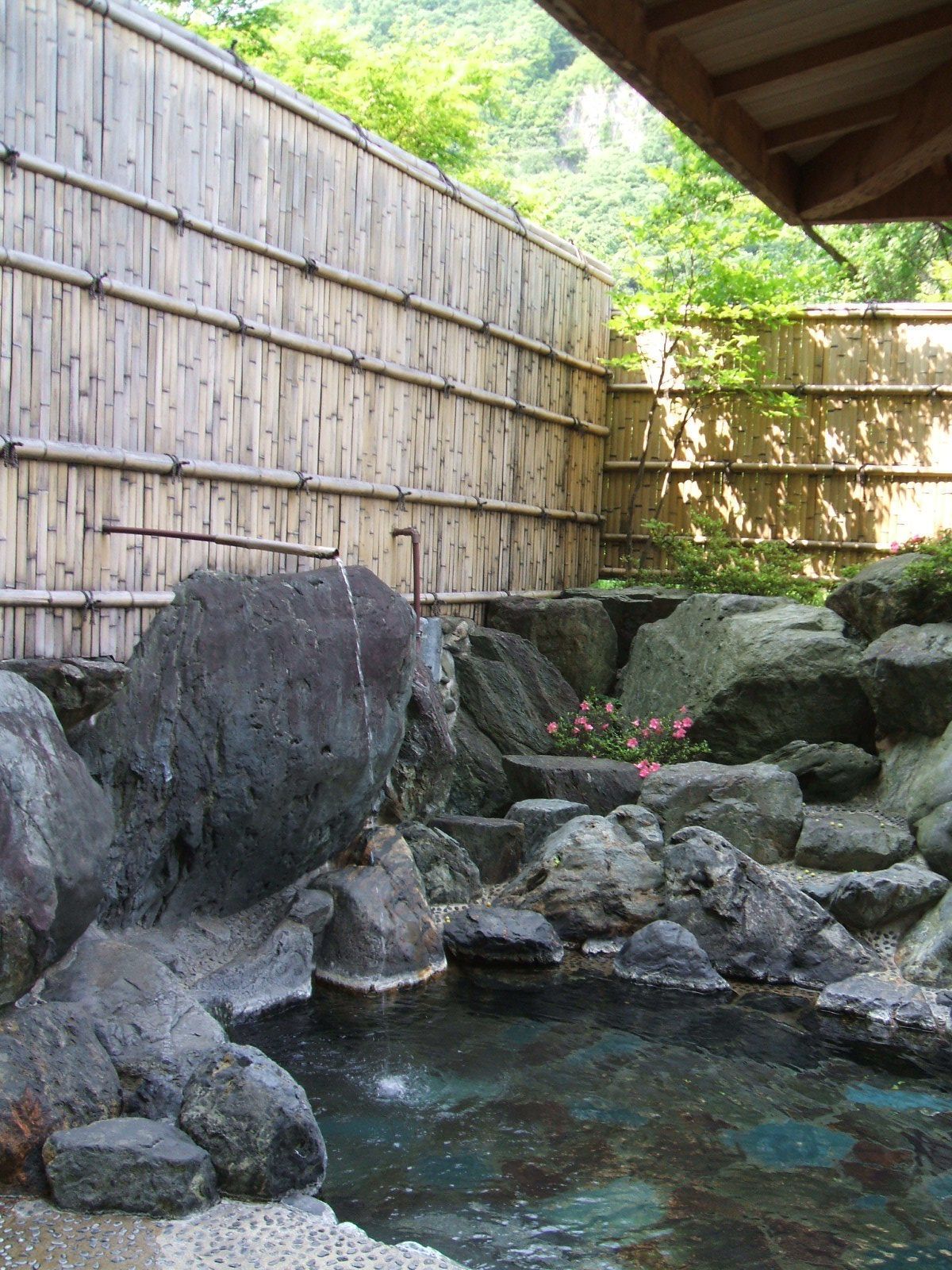 A traditional Japanese garden with a bamboo fence, large rocks, and a small pond.