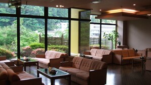 A spacious living area with multiple sofas and a coffee table, large windows offering a view of greenery and buildings outside. - Matsuriya Yuzaemon (Fukushima)