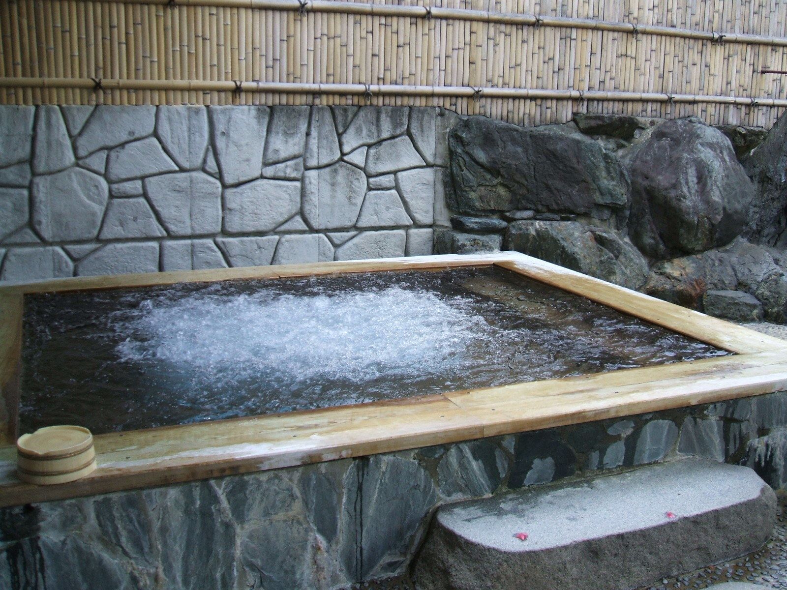 A stone wall with a wooden frame around a hot spring area.