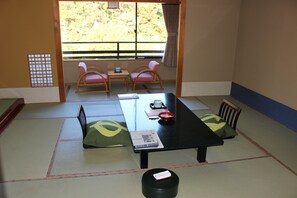 A tatami mat room with a low table, two chairs, a window with a view of greenery, and a traditional Japanese screen. - Matsuriya Yuzaemon (Fukushima)
