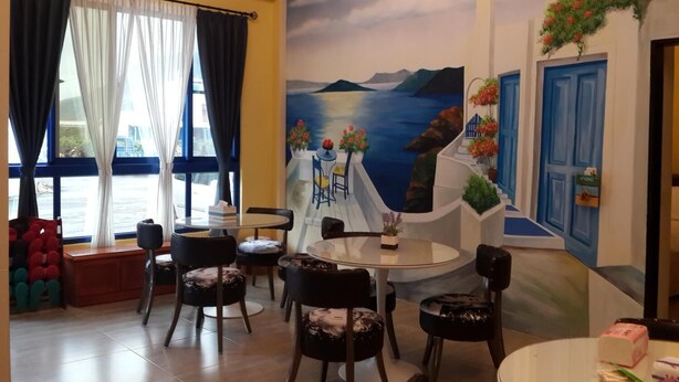 A dining area with round tables and chairs, a mural of a coastal scene, and a view of the sea through large windows with curtains. - Aegean Sea Baoli (Taitung)